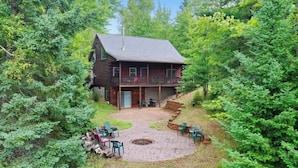 A rustic cabin with a stone patio, surrounded by dense forest. - Enjoyable 4-bedroom cabin with AC in Niagara, on a private 56 acre lake (Niagara)