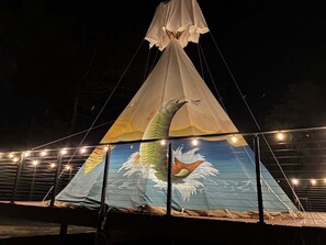 A large conical tent with a fish design on the sides, supported by a metal frame and string lights.