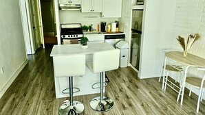 Eine moderne Küche mit weißen Schränken, einer zentralen Kochinsel inklusive Barhocker, einem eingebauten Backofen und einem Kühlschrank.