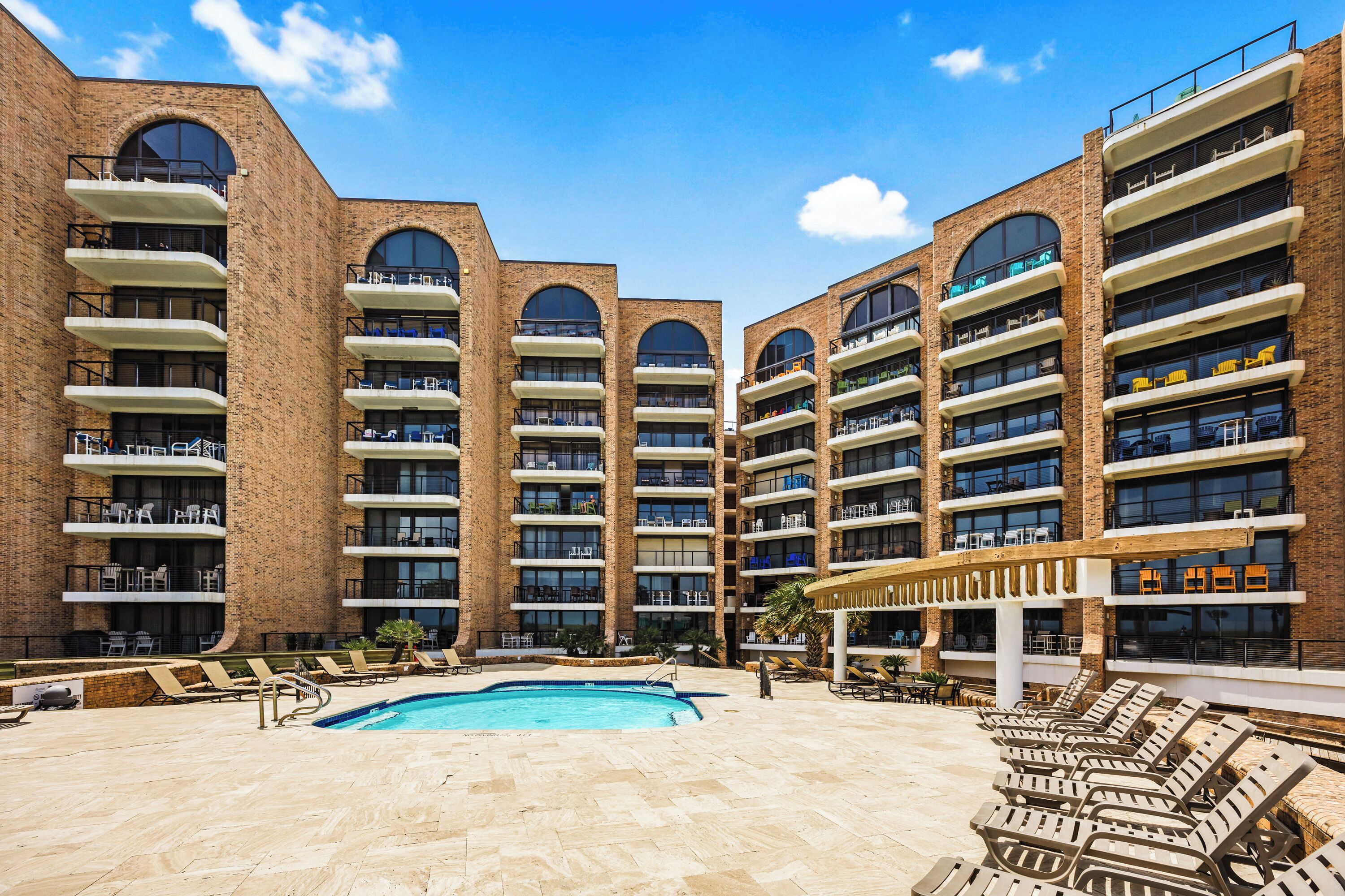 Un hotel con varios pisos, piscina exterior y tumbonas.
