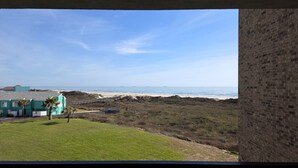 Vista costera con playa, zona de césped y un edificio con pared de ladrillo.