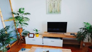 Ett vardagsrum med en tv på ett träställ, ett litet bord med en bordsduk och flera krukväxter.