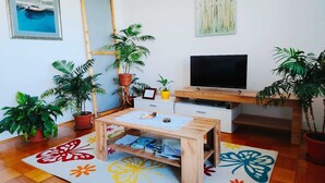 Ett mysigt vardagsrum med ett träbord, en platt-TV och flera krukväxter.