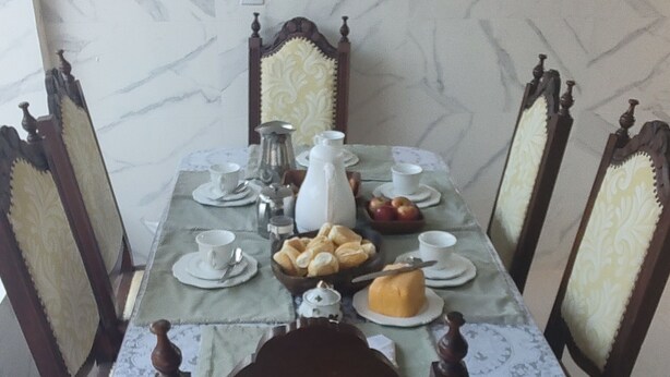A dining table set with plates, cups, and a pitcher, surrounded by chairs with patterned upholstery. - Boaventura  (Unaí)