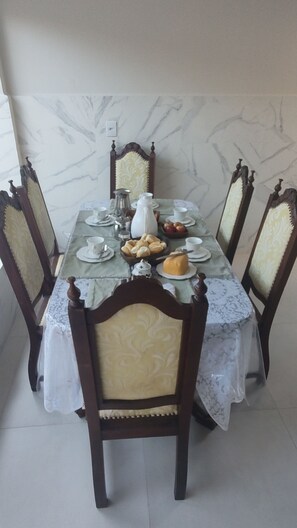 A dining table set with plates, cups, and a pitcher, surrounded by chairs with patterned upholstery. - Boaventura  (Unaí)