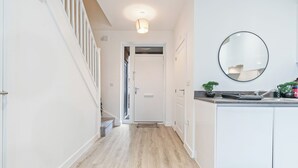 A hallway with a staircase, a white door, a kitchen area with a sink and countertop, and a round mirror on the wall. - Elegant Home | Parking | Wi-Fi | Near O2 Academy (Birmingham)