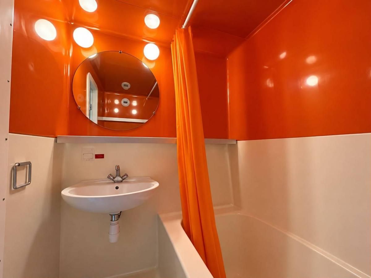 A bathroom with a white sink, a mirror, and an orange shower curtain.