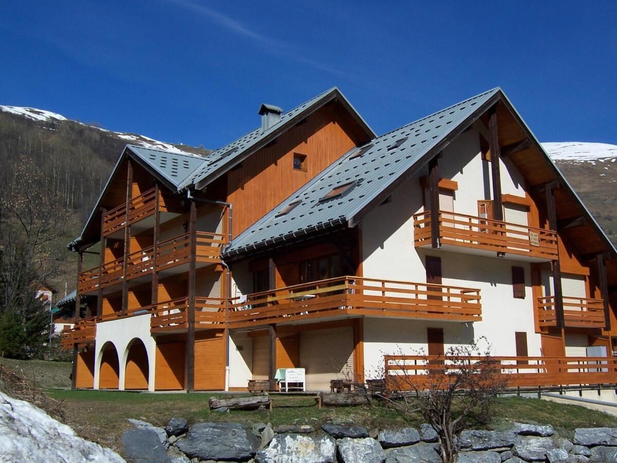 En byggnad i chalet-stil med flera balkonger, en skidlift som syns i bakgrunden och ett bergigt landskap i fonden.