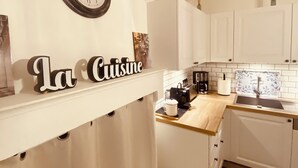 Uma cozinha com armários brancos, um relógio, uma cafeteira e uma placa que diz 'La Cuisine'.
