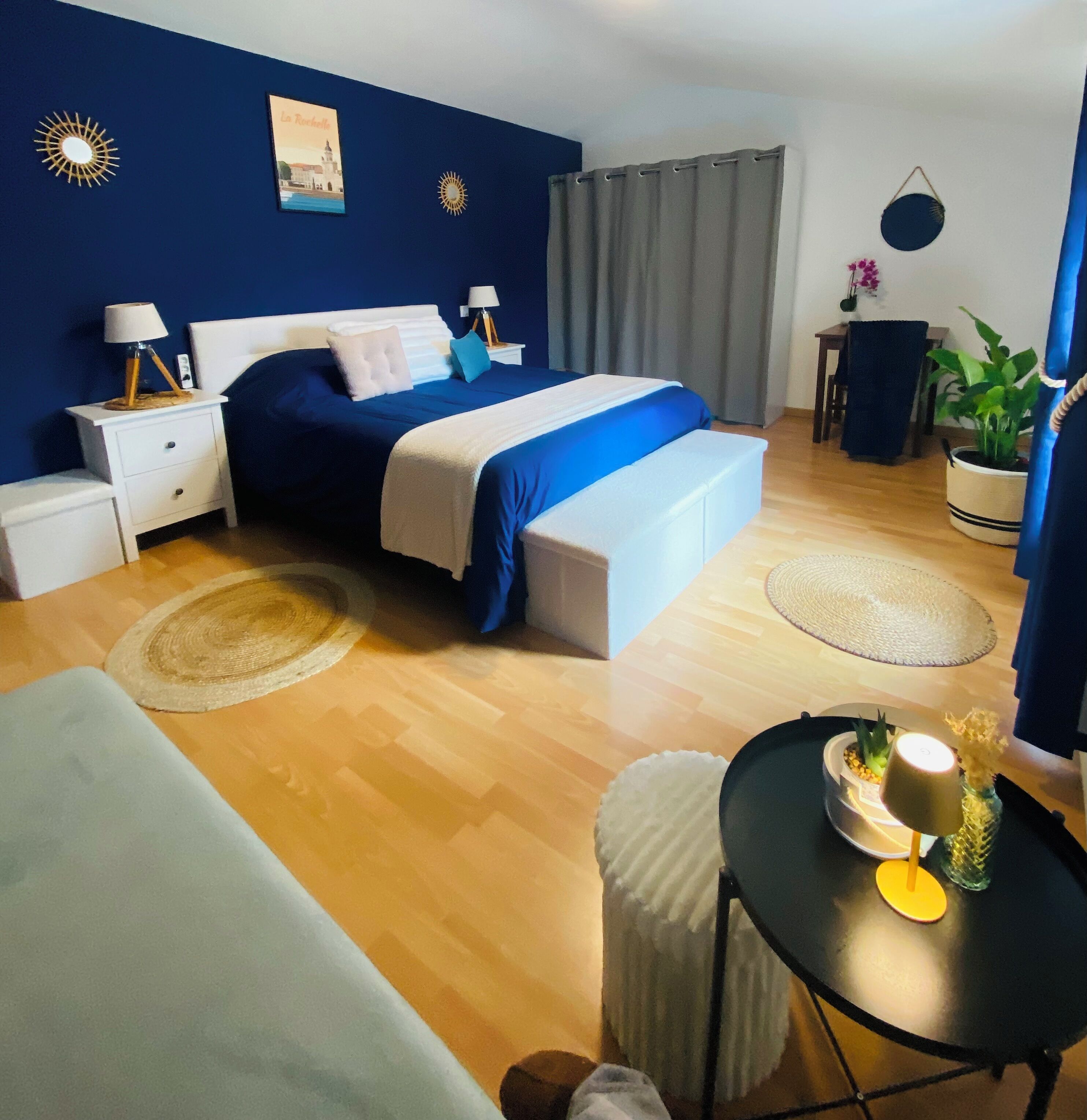 A modern bedroom with a large bed, bedside tables, a small table with a vase, and a potted plant.