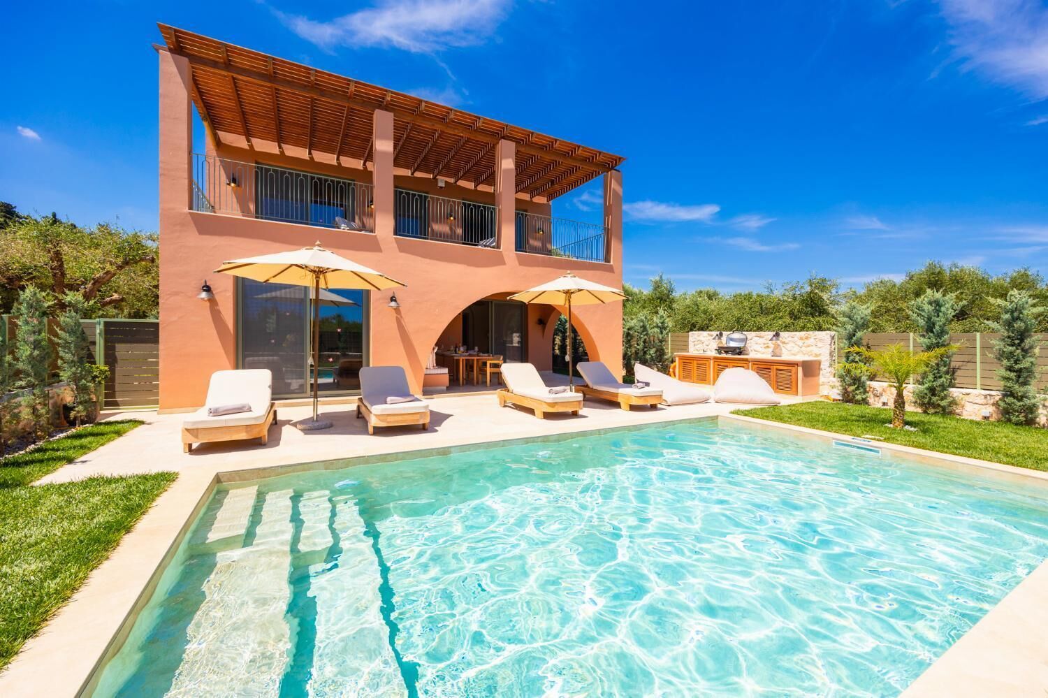 Una casa moderna de dos pisos con piscina, sillas de descanso y sombrillas.
