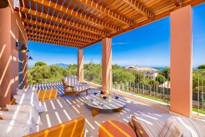 A covered outdoor seating area with a view of the sea and greenery. - Villa Analidia Supreme (Koridallos)