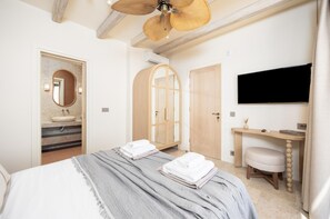 A hotel room with a bed, a vanity with a mirror, a wooden wardrobe, a desk with a chair, and a flat-screen TV mounted on the wall. - Villa Analidia Supreme (Koridallos)