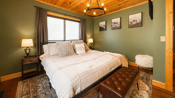 Une chambre avec un plafond en bois, un grand lit, un banc et une fenêtre avec des rideaux.