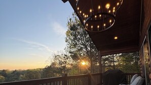 Une terrasse en bois avec une rambarde, un luminaire suspendu et une chaise.