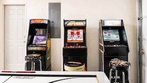 Trois bornes d’arcade proposant différents jeux, une porte blanche et, au fond, une porte de garage.