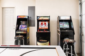 Tres máquinas de videojuegos con distintos juegos, una puerta blanca y una puerta de garaje al fondo.