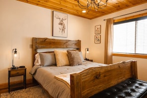 A wooden bed with a headboard, two bedside lamps, a window with blinds, and a ceiling light fixture.