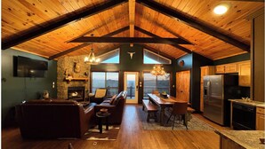 Un loft spacieux avec de hauts plafonds, des poutres apparentes, une cheminée en pierre, un coin repas et une cuisine équipée d ’appareils électroménagers modernes.