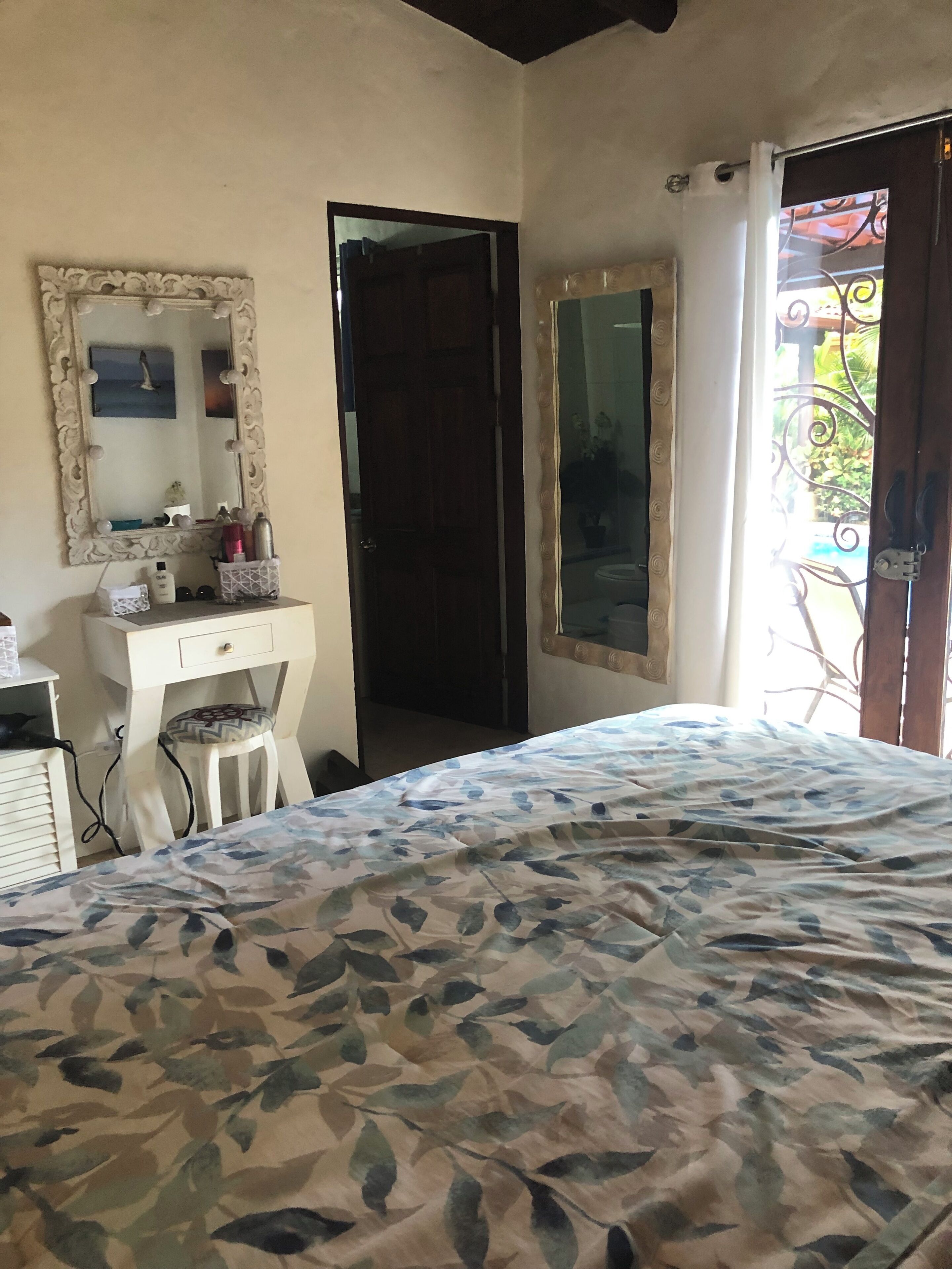 Un dormitorio con una cama, un tocador con espejo y una puerta que da a un balcón.