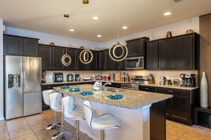 A modern kitchen with dark cabinets, stainless steel appliances, a granite island with bar stools, and pendant lighting. - Game Room|Movie Room|Free Pool Heat&BBQ|Sleeps 23 (Kissimmee)
