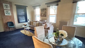 Un salon avec une table basse en verre, des canapés de couleur beige et un mur d’accent en briques.