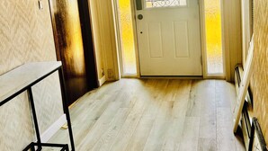 Un couloir doté d’un plancher en bois, d’une porte blanche ornée d’un panneau de verre décoratif et d’une porte en bois foncé sur la gauche.