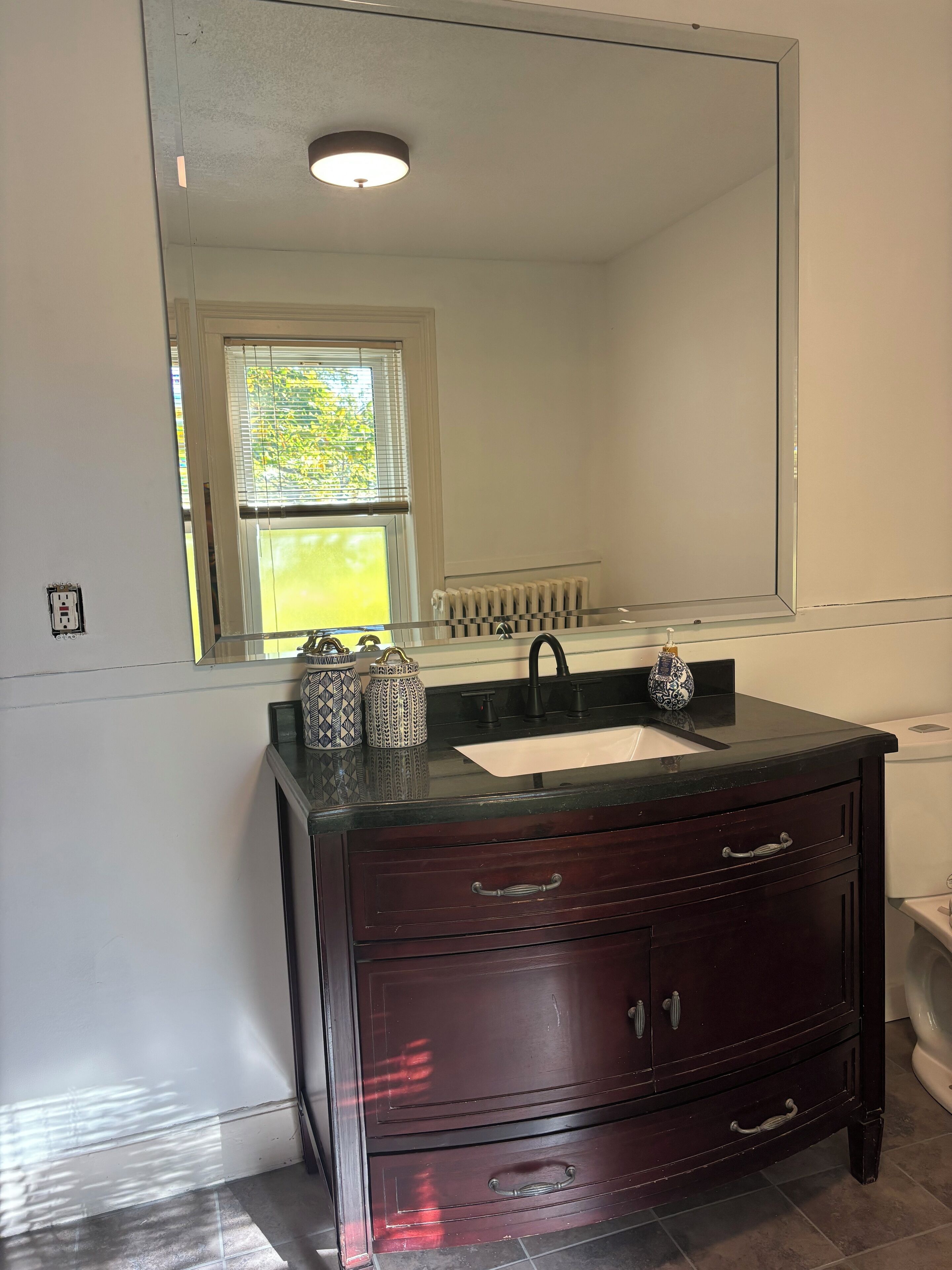 Une salle de bain avec un meuble-lavabo en bois foncé, un lavabo blanc et un grand miroir.