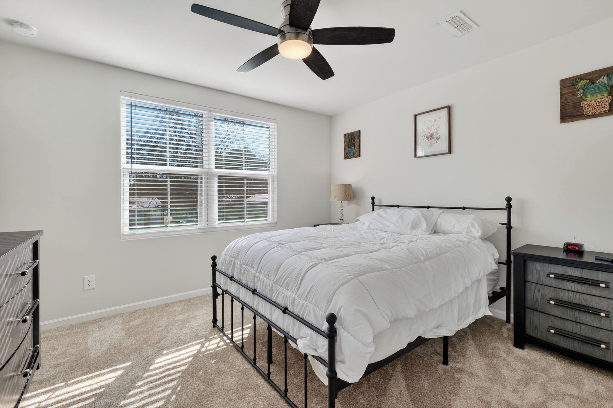 A bedroom with a bed, a dresser, a ceiling fan, and a window with blinds.