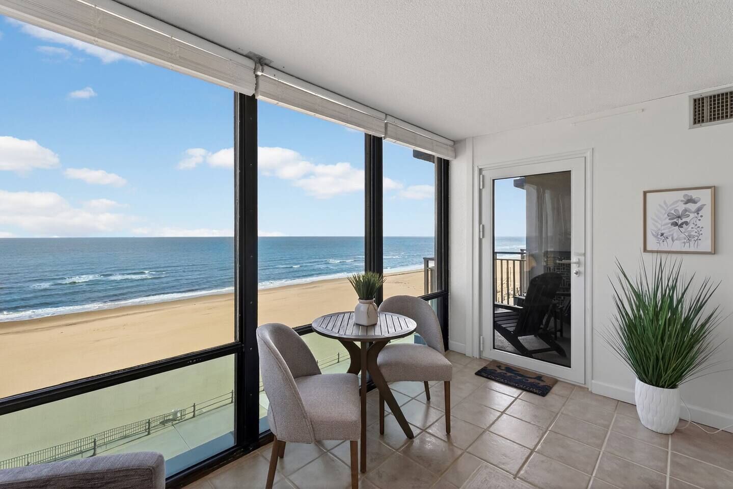 En balkon med udsigt over stranden, et bord med stole og en potteplante.