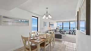 Un'ampia zona giorno con tavolo da pranzo per quattro persone, un divano grigio e vista sull'oceano.