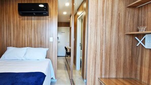 A hotel room with a bed, a wall-mounted air conditioner, a wooden wardrobe, and a small table with a glass. - COSTE0111 - Concept Life Stella (Salvador)