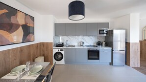 Een moderne keuken met grijze kastjes, een ingebouwde wasmachine, een roestvrijstalen koelkast en een marmeren spatwand.