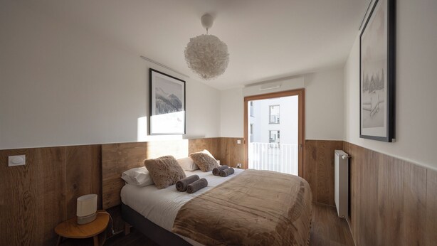 Een slaapkamer met een houten hoofdbord, een groot bed met meerdere kussens, een kleine houten stoel en een radiator.
