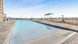Una piscina con poltrona da relax e area coperta, circondata da un vialetto in mattoni.