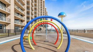 Un'area giochi con archi colorati e un elemento acquatico, sullo sfondo di un edificio a più piani.