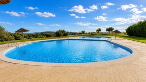 Une piscine circulaire à eau d’un bleu limpide, entourée d’une terrasse dallée.