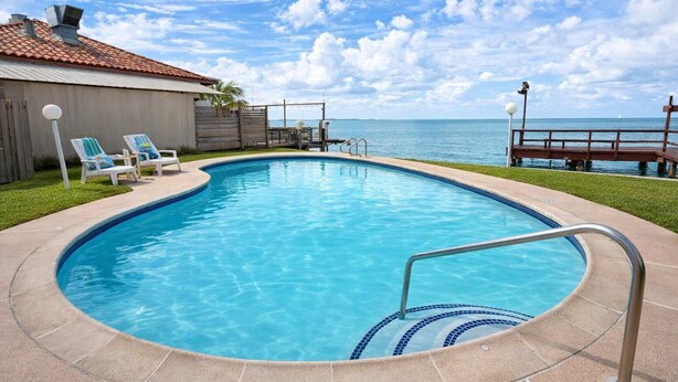 A swimming pool with a clear blue water, a wooden deck, and a view of the ocean. - Bayfront w-docks & fish 3 Patios  Prime Location (South Padre Island)