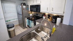 A modern kitchen with stainless steel appliances, a double sink, and a window with blinds. - Bayfront w-docks & fish 3 Patios  Prime Location (South Padre Island)