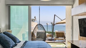 A modern bedroom with a large bed, a hanging chair, and a view of the sea. - Resort-Style Villa w/ Private Padel & Infinity Pool (Bucerías)