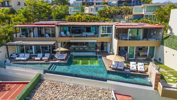 A modern multi-story building with a large swimming pool, multiple lounge areas with sunbeds, and a well-maintained garden. - Resort-Style Villa w/ Private Padel & Infinity Pool (Bucerías)