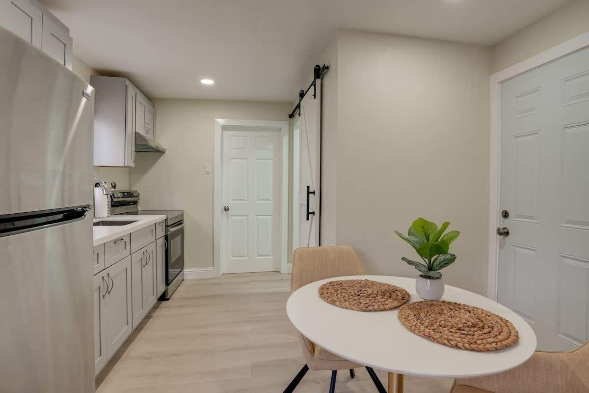 A compact kitchen with white cabinets, a white table with woven placemats, and a potted plant.