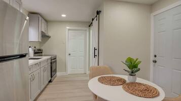 A compact kitchen with white cabinets, a white table with woven placemats, and a potted plant.