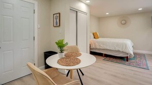Een slaapkamer met een bed, nachtkastje met een plant, een stoel, een ronde tafel en een deur.