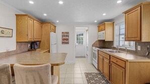 A kitchen with wooden cabinets, a granite countertop, a sink, and a dining area with chairs. - The Cozy 1 Bed / 1 Bath Duplex Near Vanderbilt Beach (Naples)