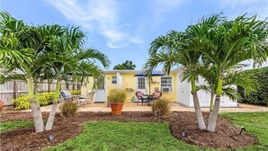 A yellow house with a patio, surrounded by palm trees and a small garden. - The Cozy 1 Bed / 1 Bath Duplex Near Vanderbilt Beach (Naples)