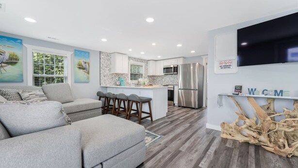 A modern living room with a grey sofa, a kitchen with white cabinets, and a bar area. - 6 Seat Golf Cart~Family Friendly~Near DT Beaufort! (Beaufort)