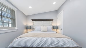 A bedroom with a bed, two bedside lamps, a window with blinds, and a door. - 6 Seat Golf Cart~Family Friendly~Near DT Beaufort! (Beaufort)