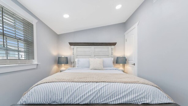 A bedroom with a bed, two bedside lamps, a window with blinds, and a door. - 4 Seat Golf Cart~Family Friendly~Near DT Beaufort! (Beaufort)
