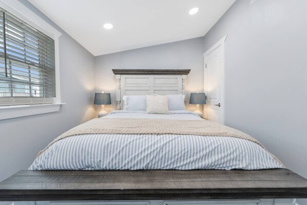Un dormitorio con una cama, dos lámparas de noche, una ventana con persianas y una puerta.